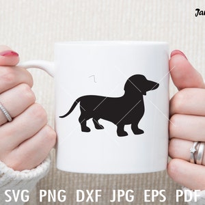 Może przedstawiać: Biały ceramiczny kubek z czarną sylwetką psa rasy dachshund. Kubek jest trzymany przez dłonie osoby.
