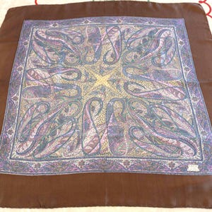 May include: A square silk scarf with a brown border and a central design featuring paisley patterns in shades of purple, blue, and yellow. The scarf is likely vintage and suitable for various occasions.