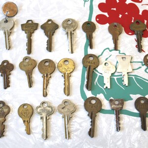 May include: A collection of vintage keys, some with brass finishes and others with silver finishes. The keys are arranged in rows on a white surface.