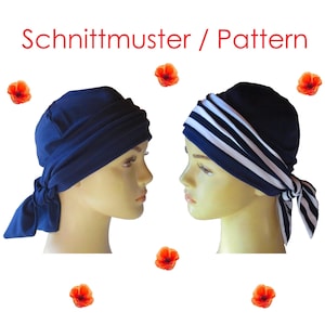 Könnte beinhalten: Zwei Kopftücher auf Schaufensterpuppenköpfen, eines in einfarbigem Marineblau und eines mit horizontalen marineblauen und weißen Streifen. Beide verfügen über seitliche Bindebänder und geraffte Stoffdetails. Der Text "Schnittmuster / Pattern" steht oben, umgeben von verstreuten roten Mohnblumen.