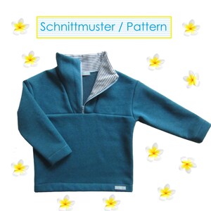 Puede incluir: Un suéter de manga larga color verde azulado con cuello alto que presenta un forro interior a rayas blancas y grises y una cremallera frontal. El texto "Schnittmuster / Pattern" aparece en la parte superior, rodeado de pequeñas flores blancas y amarillas.