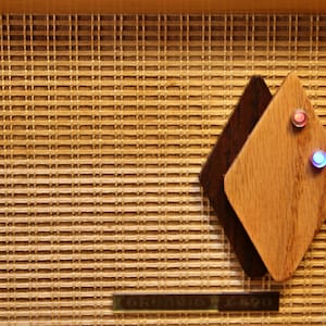 May include: Close-up of a wooden speaker grille with a diamond-shaped panel featuring two small, illuminated buttons, one red and one blue.