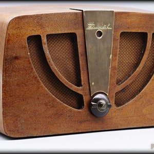 Op de afbeelding: Een vintage houten radio met een messing plaat en een zwarte knop. De radio heeft een luidsprekerrooster met een geweven stoffen patroon. De radio is gelabeld "Zenith".