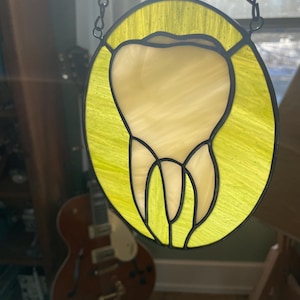 May include: A stained glass window hanging from a chain. The window is round and features a yellow background with a white tooth in the centre.