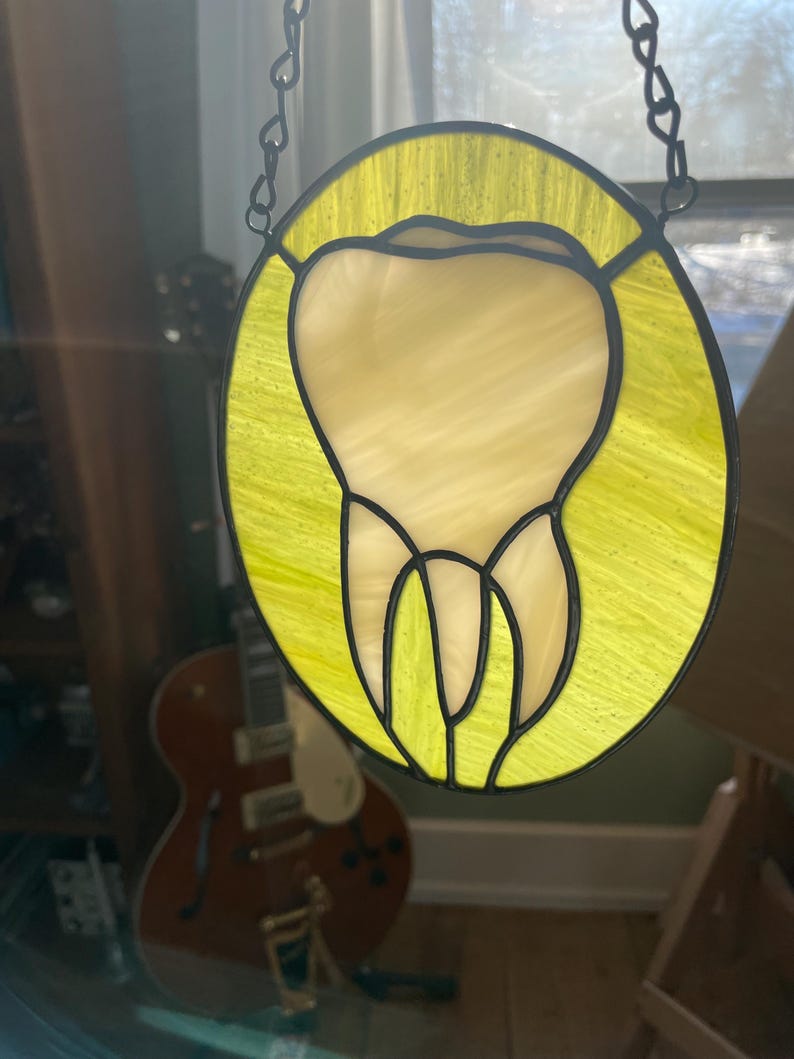 May include: A stained glass window hanging from a chain. The window is round and features a yellow background with a white tooth in the centre.