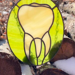 May include: A stained glass window hanging on a chain, depicting a tooth in yellow glass against a green background.