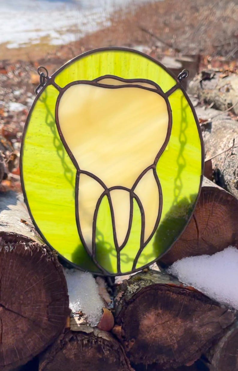 May include: A stained glass window hanging on a chain, depicting a tooth in yellow glass against a green background.