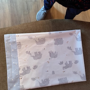 May include: White pillowcase with a repeating pattern of gray elephants, stars, and moons. The border is light blue with white stars. The pillowcase is rectangular and appears to be made of cotton.