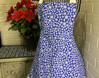 May include: A blue and white snowflake patterned apron with a white ruffle hem and halter straps. The apron is displayed on a black wire mannequin. The word "sew cute" is displayed above the apron.