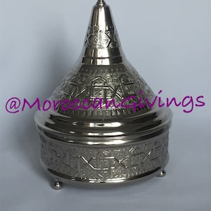 May include: A silver metal decorative box with an intricate geometric pattern. The box has a domed lid with a pointed finial.