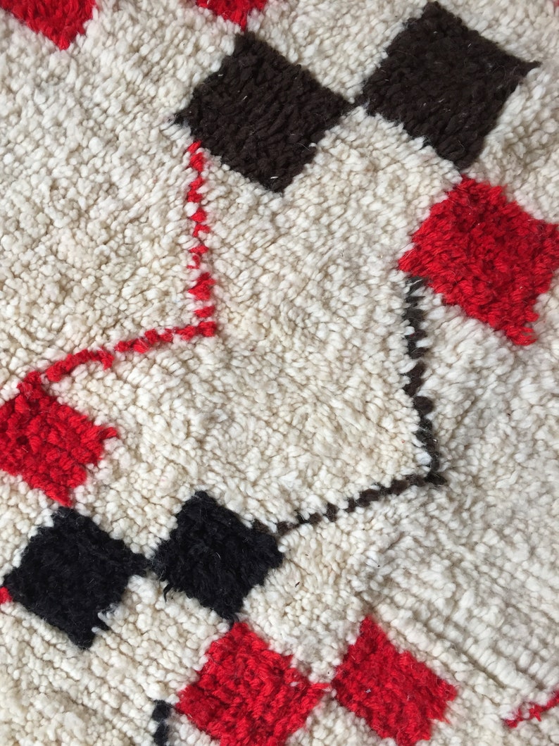 May include: A white, red, and black patterned rug with a fluffy texture. The rug has a geometric design with squares and diamonds.