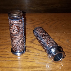 May include: A pair of brown leather motorcycle grips with a tooled floral design. The grips have a silver metal end cap.