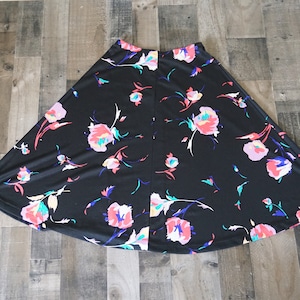 May include: Black A-line skirt with a vibrant floral pattern. The skirt features a black background adorned with pink, blue, and yellow flowers and leaves. The skirt is made of a soft, flowing fabric.