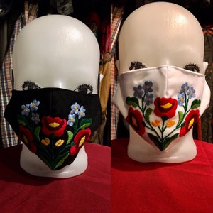 Peut inclure: Deux masques faciaux avec des motifs floraux brodés. Un masque est noir avec des fleurs rouges, blanches et bleues. L'autre masque est blanc avec des fleurs rouges, blanches et bleues.