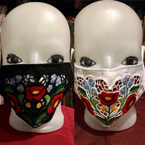 May include: Two face masks with embroidered floral designs. One mask is black with white and red flowers, the other is white with red and blue flowers.