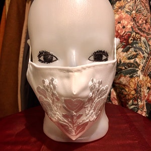 May include: White face mask with silver embroidered floral design.