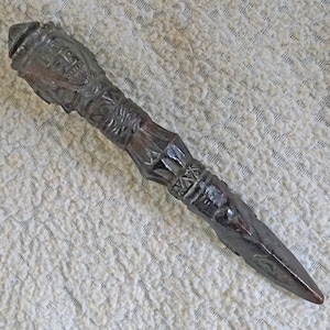 May include: A dark brown wooden dagger with intricate carvings. The handle is decorated with a human face and geometric patterns.