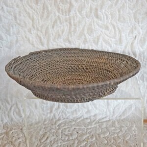 May include: A woven brown basket with a circular shape and a slightly raised rim. The basket is made of natural materials and has a rustic appearance.