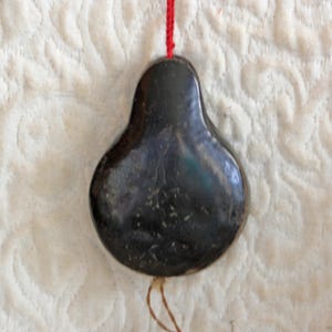 May include: A black, pear-shaped pendant with a string attached. The pendant has a smooth, glossy finish and appears to be made of metal.