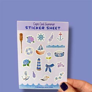 May include: A sticker sheet with a Cape Cod Summer theme. The sheet features various nautical and summer-themed illustrations, including a lighthouse, an anchor, a sailboat, a life preserver, a seagull, a captain's hat, a bow, and hydrangeas.