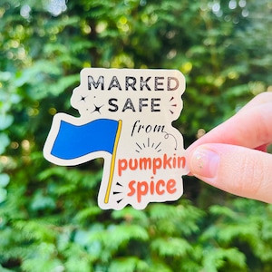 May include: A beige sticker with a blue flag and the text "MARKED SAFE from pumpkin spice".