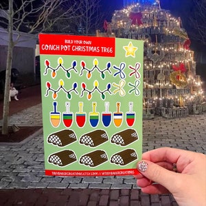 May include: Build your own Conch Pot Christmas Tree sticker sheet with colorful lights, bows, shovels, and logs.  The sticker sheet is green with a red, white, and blue border.  The text "Build your own Conch Pot Christmas Tree" is printed in white on a red background.