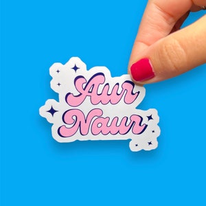 Peut inclure: Un autocollant blanc avec un lettrage rose et bleu qui dit "Aur Naur" avec de petites &eacute;toiles blanches autour du texte.