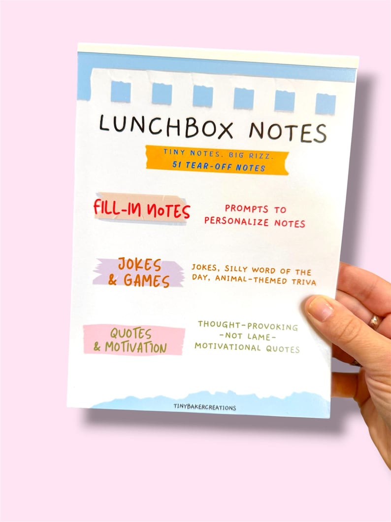 Może przedstawiać: Biały notatnik Lunchbox Notes z niebieskimi i ż&oacute;łtymi akcentami trzymany w dłoni. Notatnik zawiera tekst, w tym "Lunchbox Notes", "Fill-in Notes", "Jokes & Games" i "Quotes & Motivation". Notatnik zawiera 51 karteczek.