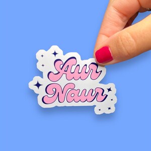 Peut inclure: Un autocollant blanc avec un lettrage rose et bleu qui dit "Aur Naur" avec de petites &eacute;toiles blanches autour du texte.