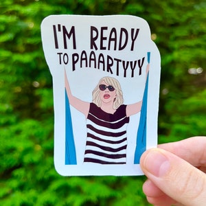 May include: A white sticker with a cartoon illustration of a woman with blonde hair wearing sunglasses and a black and white striped shirt. The woman is holding onto two blue curtains. The text on the sticker reads "I'm ready to paaartyyy".
