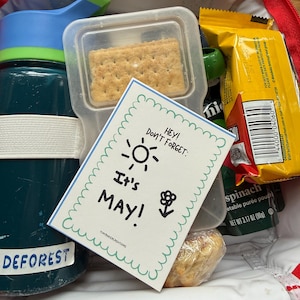 Może przedstawiać: Czerwono-niebieska torba na lunch wypełniona przekąskami i butelką wody. Torba zawiera przezroczysty pojemnik z krakersem, saszetkę ze szpinakiem i kartkę z napisem "Hey! Don't Forget: It's MAY!" i "TINYBAKERCREATIONS".