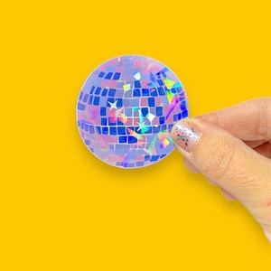 May include: A holographic disco ball sticker with a blue, purple, and pink iridescent finish. The sticker is round and has a textured surface.