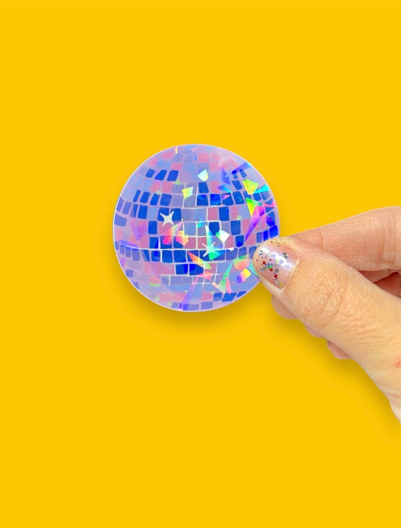 May include: A holographic disco ball sticker with a blue, purple, and pink iridescent finish. The sticker is round and has a textured surface.