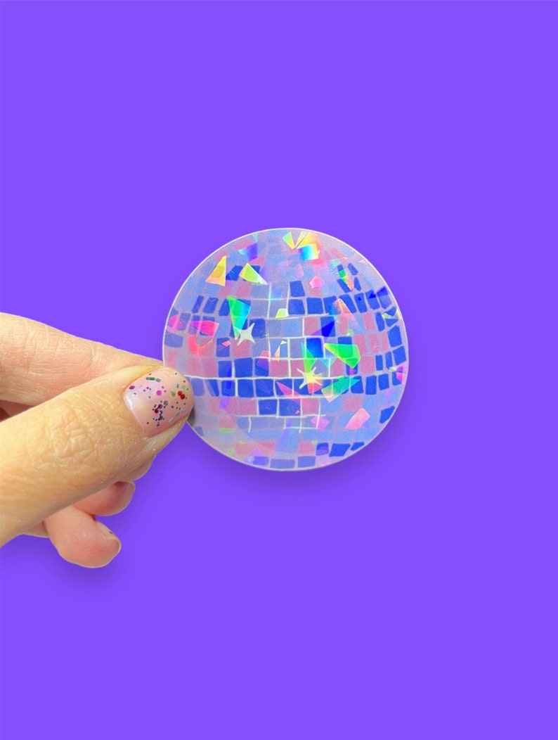 May include: A clear iridescent disco ball sticker with a holographic finish. The sticker has a grid pattern and is decorated with small, colorful, iridescent pieces.