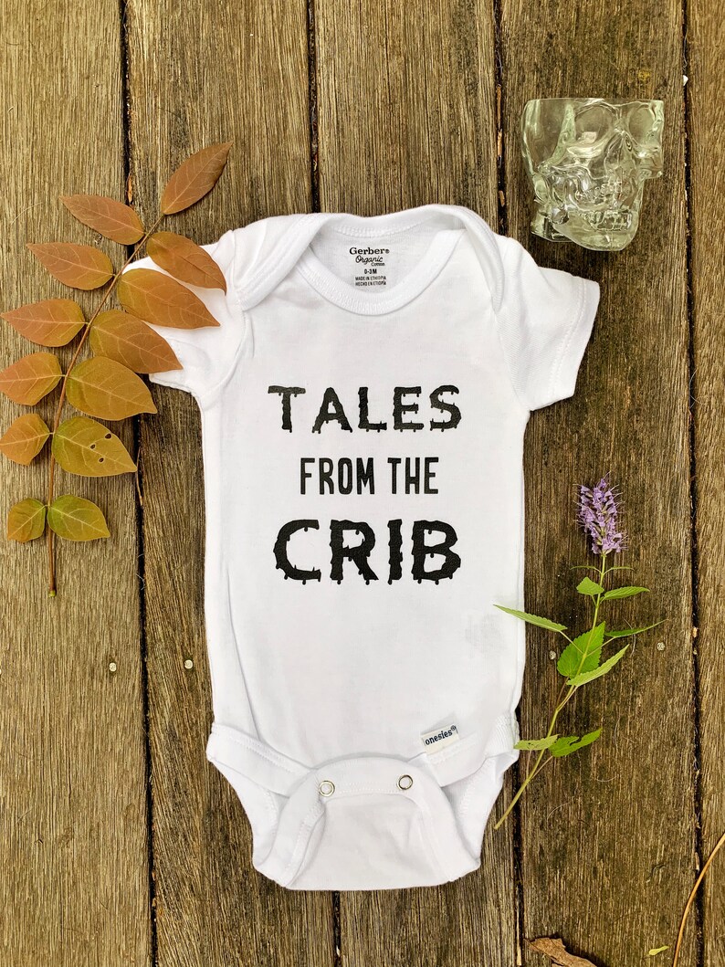 K&ouml;nnte beinhalten: Wei&szlig;er Baby-Strampler mit schwarzem Text, der "Tales from the Crib" lautet.