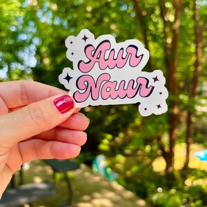 Peut inclure: Un autocollant rose et noir avec le texte "Awr Naur" dans une police r&eacute;tro. L'autocollant a deux petites &eacute;toiles noires de chaque c&ocirc;t&eacute; du texte.