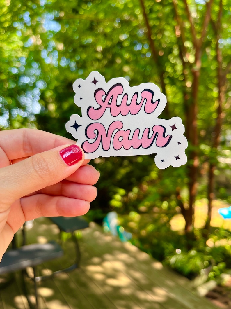 Peut inclure: Un autocollant rose et noir avec le texte "Awr Naur" dans une police r&eacute;tro. L'autocollant a deux petites &eacute;toiles noires de chaque c&ocirc;t&eacute; du texte.