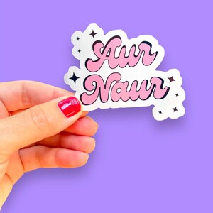 Peut inclure: Un autocollant rose et blanc avec le texte "Awr Naur" dans un style de police r&eacute;tro. L'autocollant a de petits accents d'&eacute;toiles.