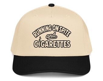 Könnte beinhalten: Eine beigefarbene Baseballkappe mit schwarzem Schirm und einem schwarzen Knopf oben. Auf der Vorderseite befindet sich eine schwarze Stickerei mit dem Text RUNNING ON SPITE and CIGARETTES, wobei eine Zigarette den Buchstaben I ersetzt.