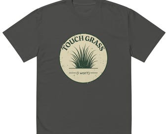 Könnte beinhalten: Ein dunkel anthrazitfarbenes Kurzarm-T-Shirt mit einer kreisförmigen Grafik auf der Brust. Die Grafik hat einen cremefarbenen Hintergrund, eine dunkelgrüne Abbildung eines Grasbüschels, den Text "TOUCH GRASS" darüber und "(I won't)" darunter.