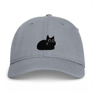 May include: A grey baseball cap featuring a centred graphic of a solid black cat silhouette. The cat design includes simple white outlines for the eyes and three thin white lines on each side of the face to represent whiskers on the feline figure.