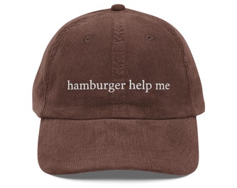 Könnte beinhalten: Eine braune Baseballkappe aus Cord mit dem gestickten weißen Text "hamburger help me" mittig auf der Vorderseite. Die Kappe hat eine strukturierte Krone, einen gebogenen Schirm und genähte Ösen zur Belüftung auf den oberen Paneelen.