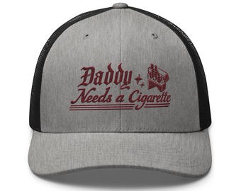 Könnte beinhalten: Eine Baseballkappe in Grau meliert mit schwarzem Netzrücken und verstellbarem Verschluss. Die Vorderseite zeigt eine dunkelrote Stickerei mit dem Schriftzug "Daddy Needs a Cigarette" in gotischer Schrift und ein kleines Zigarettenpackungs-Motiv.