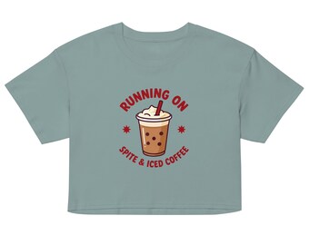Könnte beinhalten: Ein salbeigrünes bauchfreies T-Shirt mit einer zentralen Grafik eines Eiskaffees mit Schlagsahne und einem roten Strohhalm. Der Text um die Illustration lautet "RUNNING ON SPITE & ICED COFFEE" in roten Großbuchstaben, ergänzt durch zwei kleine rote Sternsymbole.