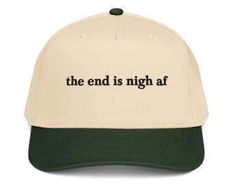 Könnte beinhalten: Eine cremefarbene Baseballkappe mit dunkelgrünem Schirm und einem dunkelgrünen Knopf an der Oberseite. Auf der Vorderseite der Kappe befindet sich der schwarz gestickte Text "the end is nigh af" in einer Serifenschrift. Die Kappe hat eine strukturierte Krone.