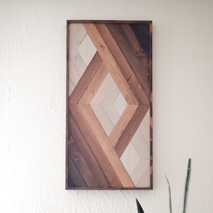 Puede incluir: Una pieza de arte de pared geom&eacute;trica hecha de madera con un patr&oacute;n de diamante. La madera est&aacute; te&ntilde;ida en tonos de marr&oacute;n y blanco.
