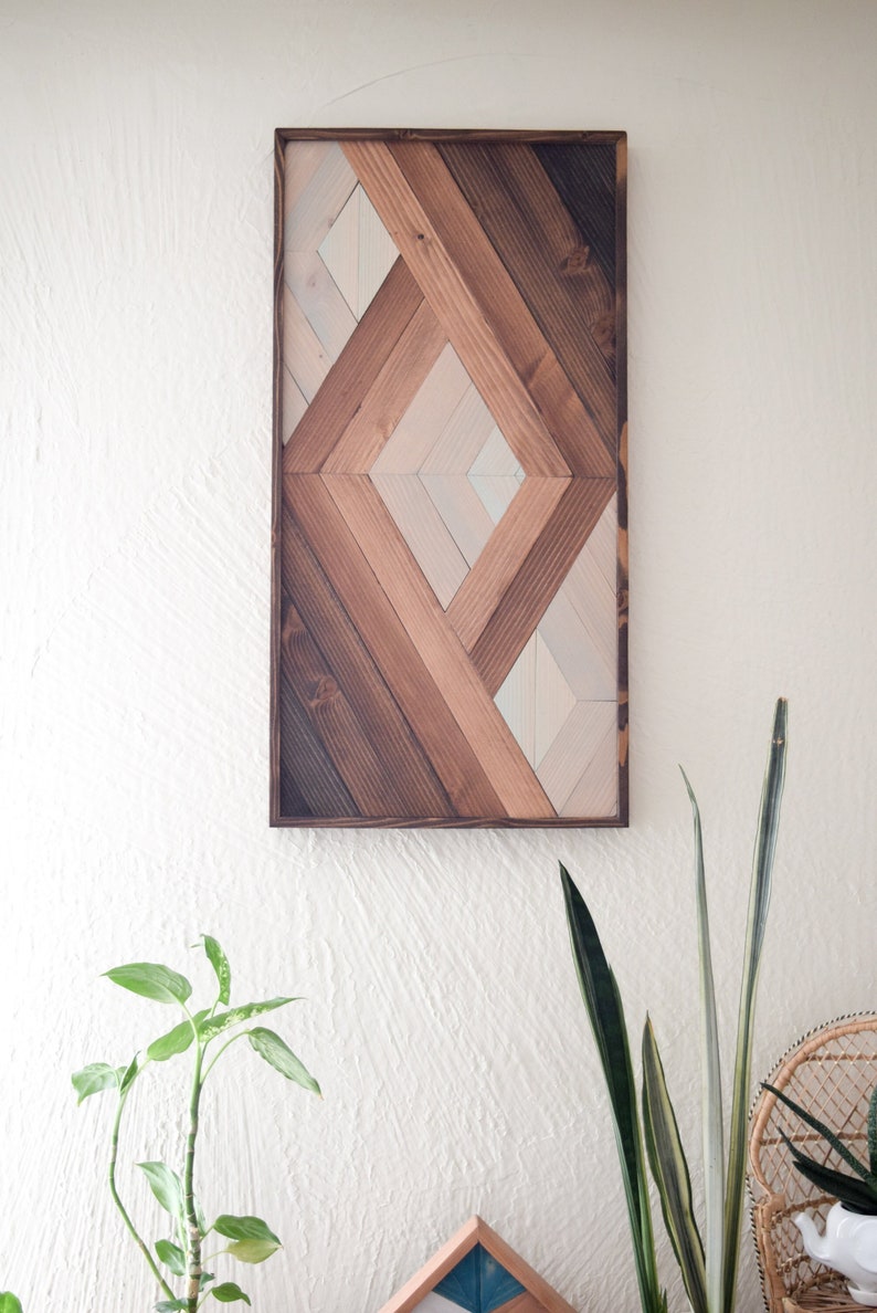 Puede incluir: Una pieza de arte de pared geom&eacute;trica hecha de madera con un patr&oacute;n de diamante. La madera est&aacute; te&ntilde;ida en tonos de marr&oacute;n y blanco.
