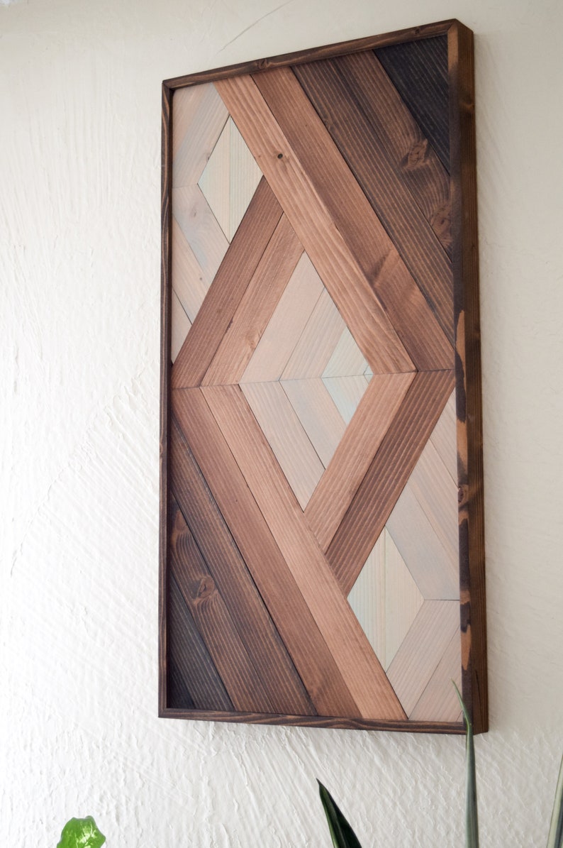 Puede incluir: Una pieza de arte de pared geom&eacute;trica hecha de madera con un patr&oacute;n de diamante. La madera est&aacute; te&ntilde;ida en varios tonos de marr&oacute;n y blanco.