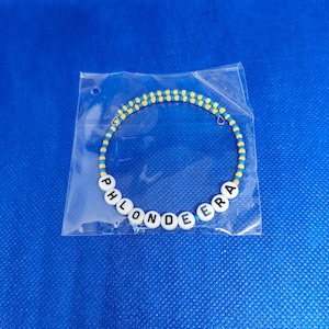 May include: A blue and yellow beaded bracelet with the word "PHLONDEERA" spelled out in white beads.