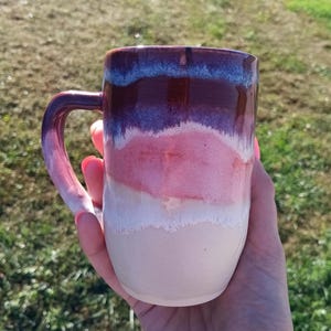 May include: A ceramic mug featuring a smooth, glossy glaze with a layered color gradient. The top section is a deep dark purple, transitioning into a vibrant pink middle band, and finishing with a light cream base at the bottom.
